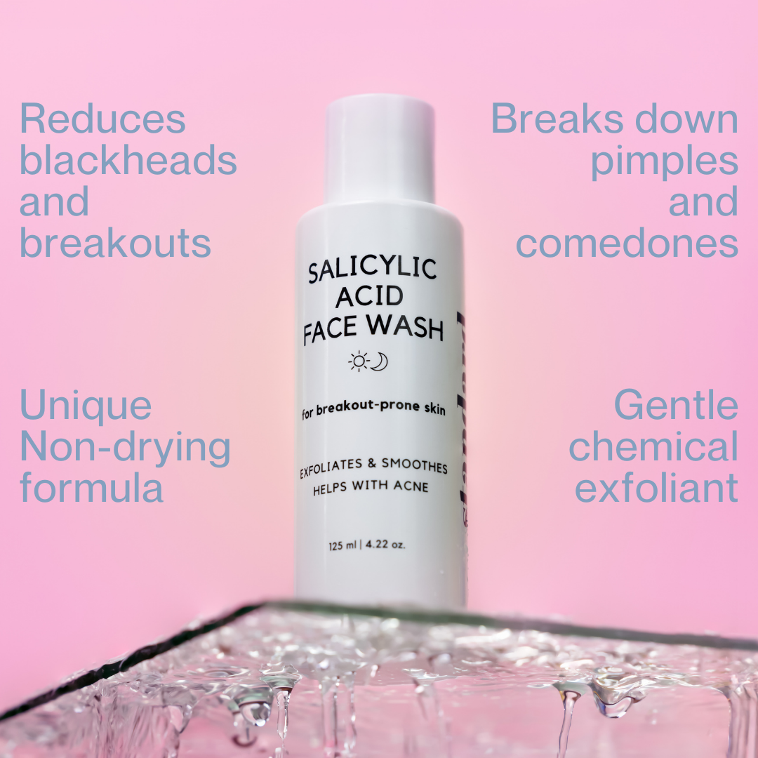 A bottle of Standard Beauty Salicylic Acid Face Wash designed for breakout-prone skin, indicating it helps with acne and exfoliates skin. The bottle is on a glass surface in water.