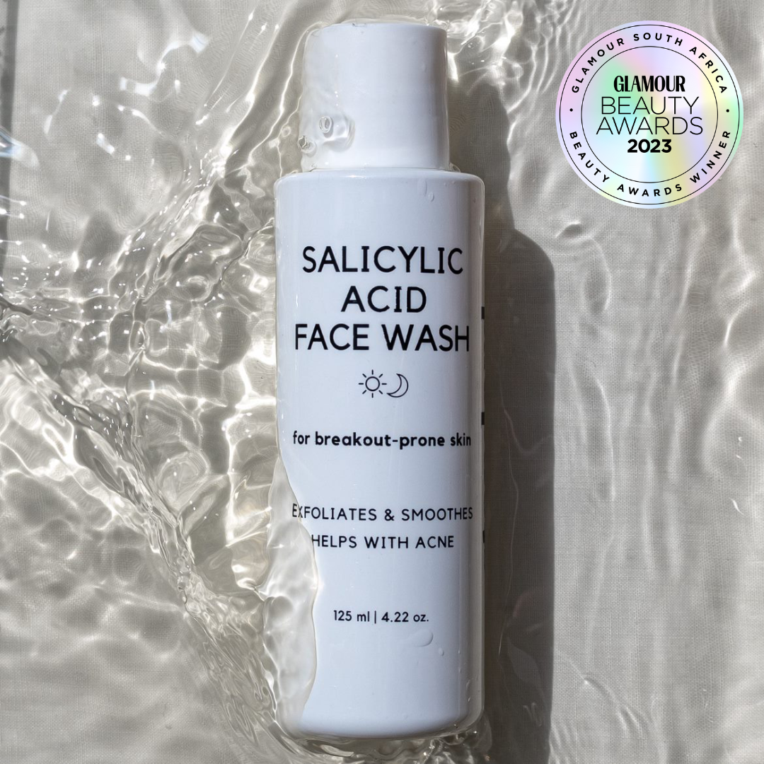 A bottle of Standard Beauty Salicylic Acid Face Wash designed for breakout-prone skin, indicating it helps with acne and exfoliates skin. The bottle is in water.